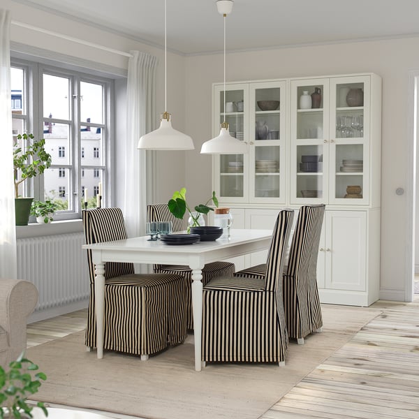 Modern minimalist dining area with extendable table, striped chairs, glass cabinet, and large window. Bright & clean.