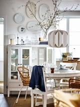 Bright dining space with white INGATORP extendable table, wicker chairs, glass cabinet, and wall-mounted plates. Modern, clean design.