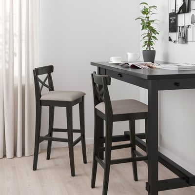 Modern black INGOLF bar stool with cushioned seat in minimalist kitchen under table with plant, cups, and magazines.