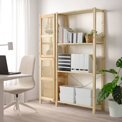 A light-colored wooden bookshelf with open and closed storage, featuring a laptop on a desk and a green plant.