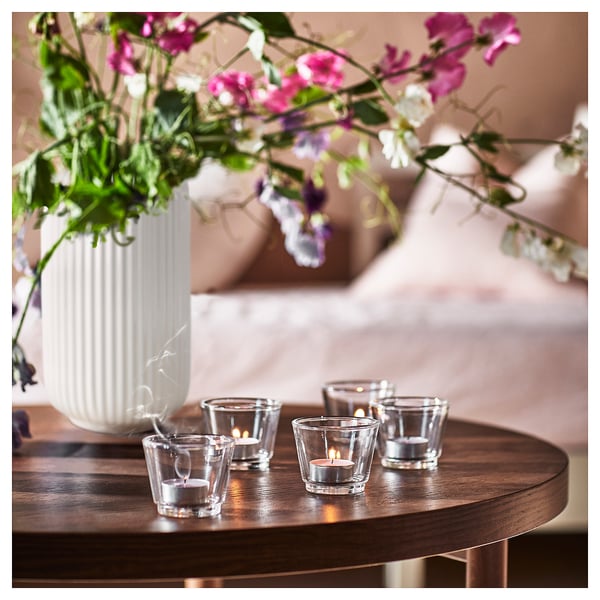 Four lit candles on wooden table with floral arrangement.