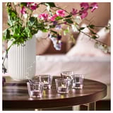 Four lit candles on wooden table with floral arrangement.