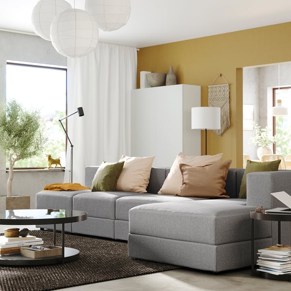 Modern living room with JÄTTEBO gray sectional sofa, colorful pillows, sleek coffee table, and large window with curtains.