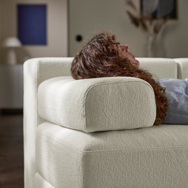 A person relaxes on a plush, white modular sofa, using a headrest for comfort, showcasing its versatile support function.