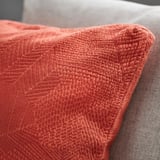 Close-up of textured red-orange cushion cover with leafy pattern, boxed corners.