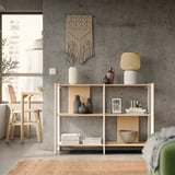 Modern living room: gray JÄTTESTA shelf with vases, books, and green rug. Concrete wall, macrame, and wooden chairs.
