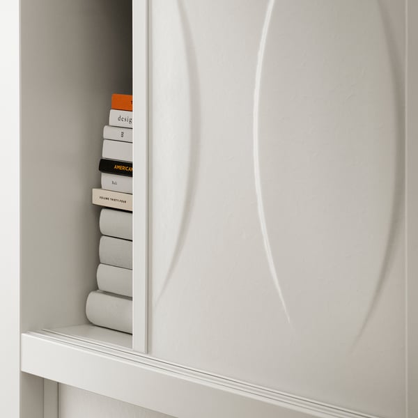 White KALKNÄS cabinet with sliding glass doors, showing neatly stacked books. Modern, minimalist design.