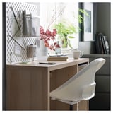 Modern wooden desk with white chair, organized with storage baskets and decor.