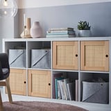 KALLAX shelf unit with woven doors, gray felt boxes, decorative items.