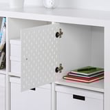 White KALLAX shelf insert with hole-filled door, using pegboard function, holding notebooks and pens.