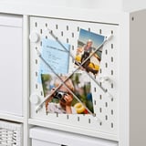 White KALLAX shelf with pegboard door, displaying photos and notes, for personalized storage and organization.