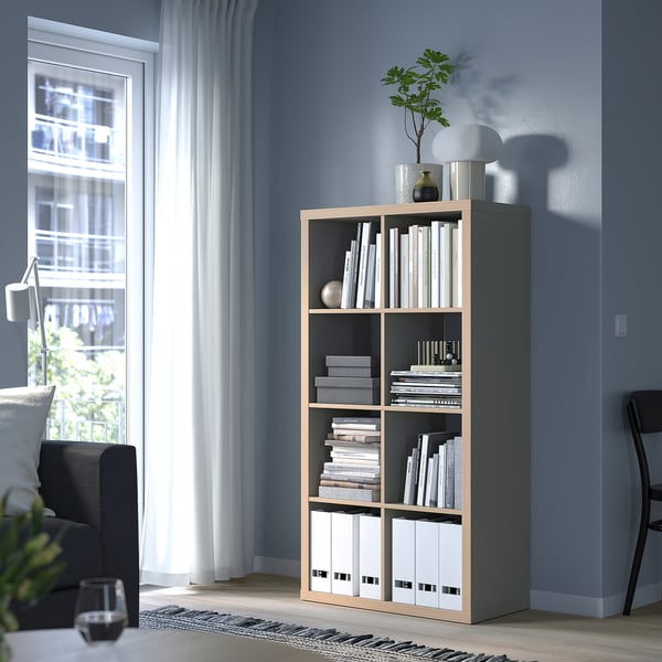 KALLAX bookshelf with books and decor, beside gray couch and black chair, against blue wall.