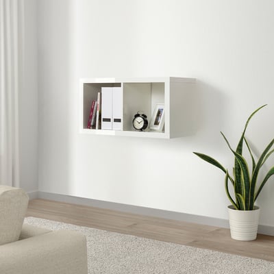 KALLAX white wall shelf, glossy finish, wooden base, rectangular shape, minimalist design, holds books, clock, frame, potted plant against plain wall.