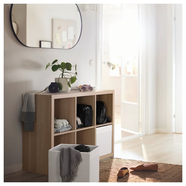 Modern hallway with IKEA KALLAX shelving, bags, towels, plants, mirror, and natural light.