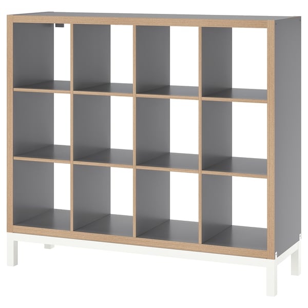 An empty KALLAX shelving unit in grey and light wood. It multiple cubes for storage, supported by a white underframe.