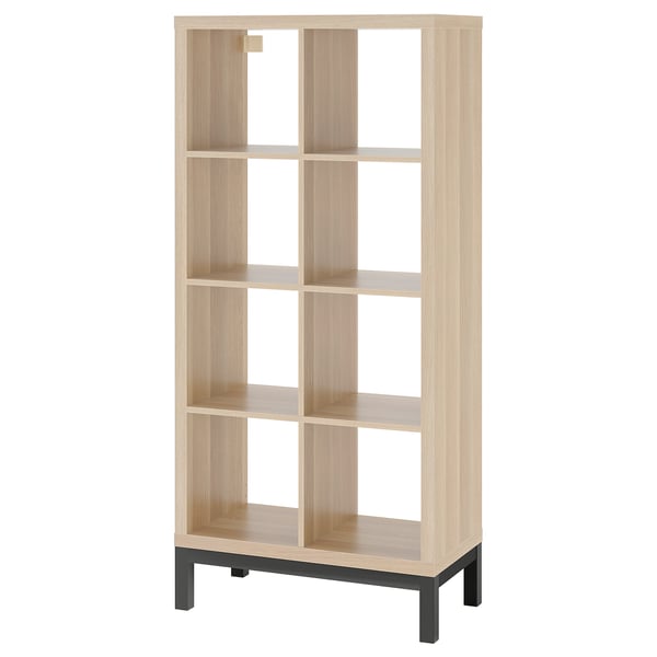 The KALLAX is a light oak, wooden bookshelf with a black metal base, featuring open compartments for versatile storage and display.