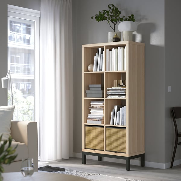 KALLAX bookcase with books and decor, by window with curtains. Includes chair and desk.