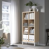 KALLAX bookshelf in light oak with white boxes, near a window. Modern, elevated, holding books & decor.