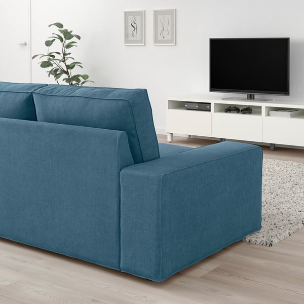 Modern living room with KIVIK blue sofa, large flat screen tv on stand, decorative plant, minimalistic art, light-colored rug, and wooden floor.