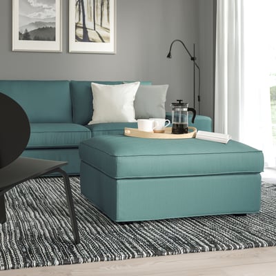 KIVIK footstool in teal, with storage, sits in a cozy living room. Its size complements the matching sofa and rug. Decorative tray on top.