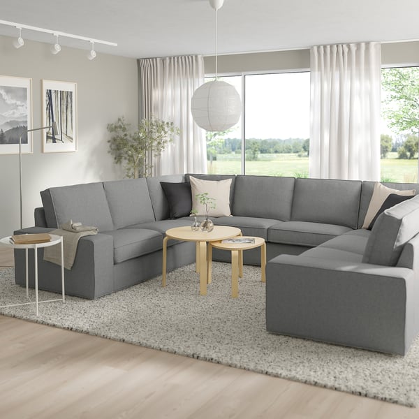 Modern grey KIVIK sectional sofa in large room, with low armrests, deep cushions, wooden side tables, and floor lamp.
