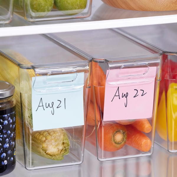 Clear fridge containers with lids and dates on labels store fresh produce, organized with written dates.
