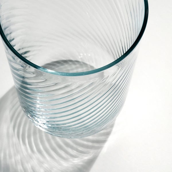Close-up of a sleek, clear glass with a smooth exterior and textured interior, casting intricate shadows, highlighting its delicate quality.