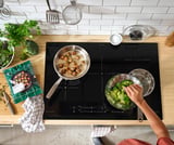 Cooking scene: black stovetop with pots of food, vegetables, and cookbooks.