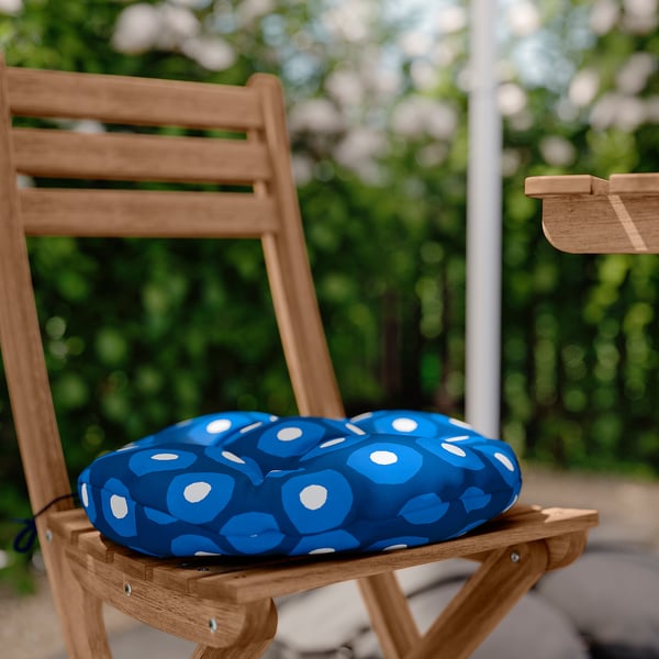 Blue circular patio chair cushion with white polka dots on a wooden chair. Recycled polyester material.