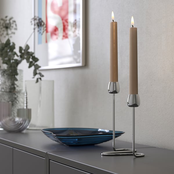 KLOKHET candles, silver holder, two beige candles on modern cabinet, small bowl, decorative vase left, art on wall, cozy living room setup.
