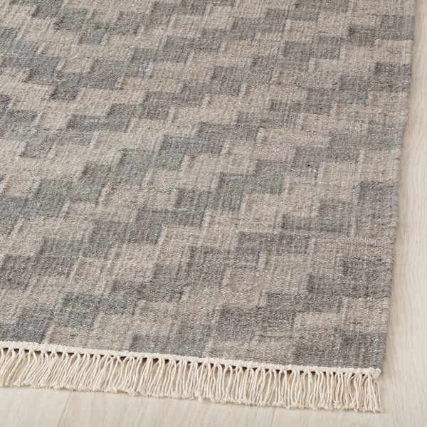 High-quality, handwoven rug on wood floor. Intricate gray patterns, durable wool, cream fringes.