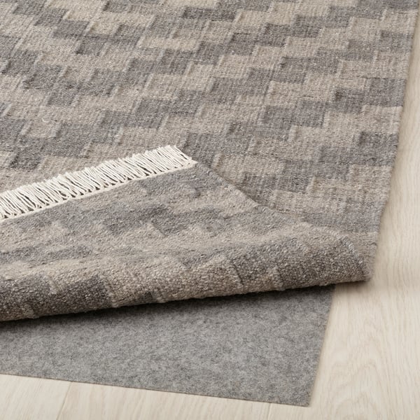 Grey wool rug, handwoven with fringed edges, displayed on light wood floor.