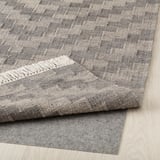 Grey wool rug, handwoven with fringed edges, displayed on light wood floor.
