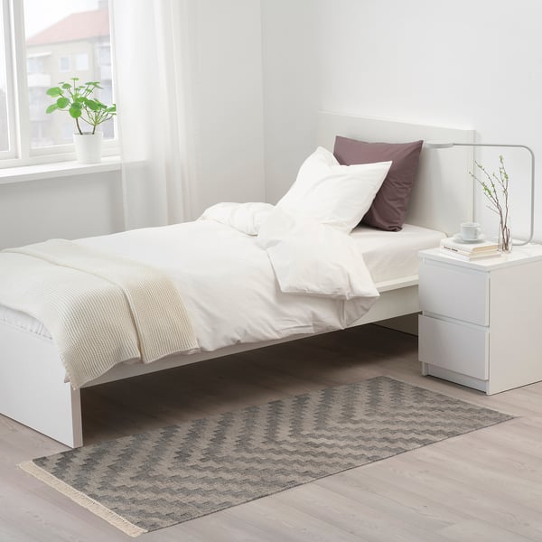 KNAPPHIRS grey zigzag rug in bedroom under bed, next to nightstand, with fringe.