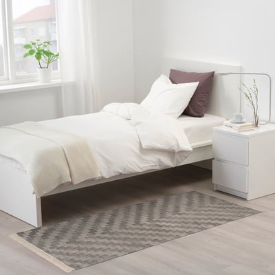 KNAPPHIRS grey zigzag rug in bedroom under bed, next to nightstand, with fringe.