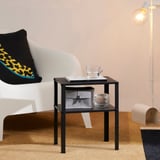 Black bedside table next to white couch, holding a cup and a book. Supported by metal bars, providing storage underneath.