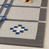 Handwoven rug featuring geometric patterns and varied textures. Neutral colors with blue accents. Wool material, durable and soft.