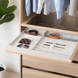 Open wooden drawer with pulled-out tray holding belts, ties, and watches in compartments. Felt lining protects accessories.