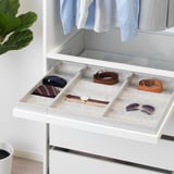 White wardrobe drawer with gray felt inserts organizing accessories: belts, ties, watch, and sunglasses.