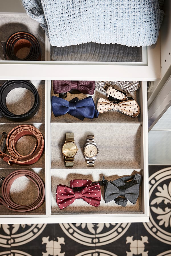 KOMPLEMENT drawer with white tray, felt inserts, blue sweater, belts, watches, and bow ties neatly organized.
