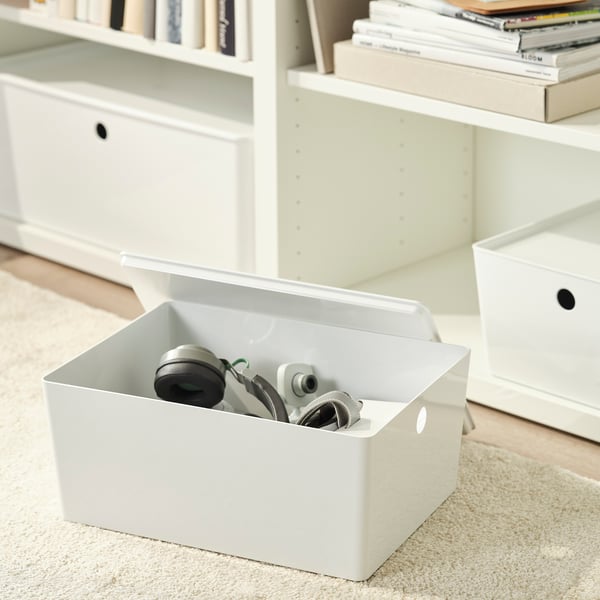 White box with cables and gadgets on carpet, bookshelf in background.