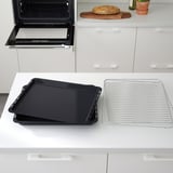 Black baking tray and wire rack sit on white countertop near open, modern oven.
