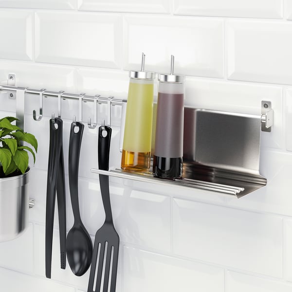 Metal kitchen shelf with hooks holding black utensils and glass containers.