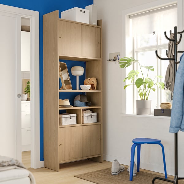 Modern entryway with light wood LÅDMAKARE cabinet, blue accents, plant, and coat rack.