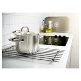 Silver saucepan with lid sits on metallic trivet over kitchen sink and stove.