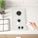 Hand cleans a sleek, modern gas hob with two burners, knobs for control.