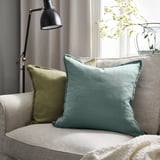 Couch with light blue LAGERPOPPEL pillow, green pillow, white flowers, lamp.