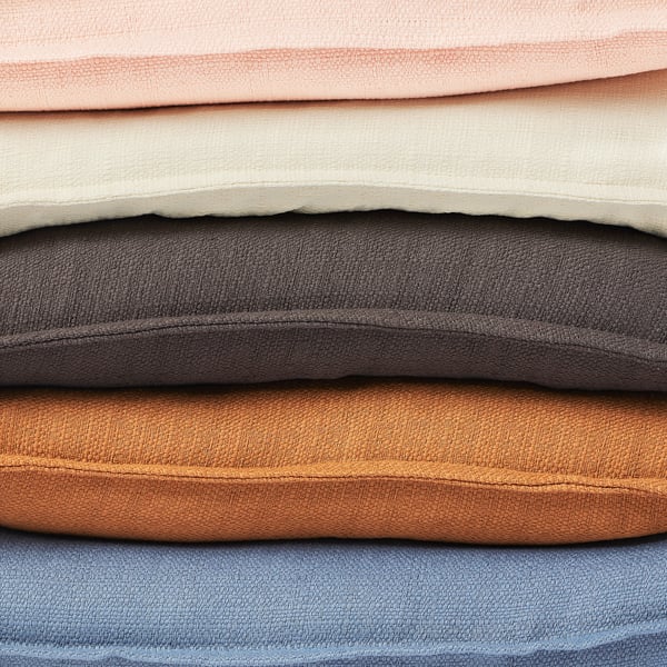 A stack of foldable fabrics in various colors including peach, beige, gray, brown, and blue. Each piece has a textured surface and simple edge design.