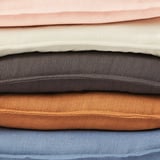 A stack of foldable fabrics in various colors including peach, beige, gray, brown, and blue. Each piece has a textured surface and simple edge design.