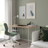 Minimalist home office with LAGKAPTEN desk, laptop, lamp, posters, and chairs.